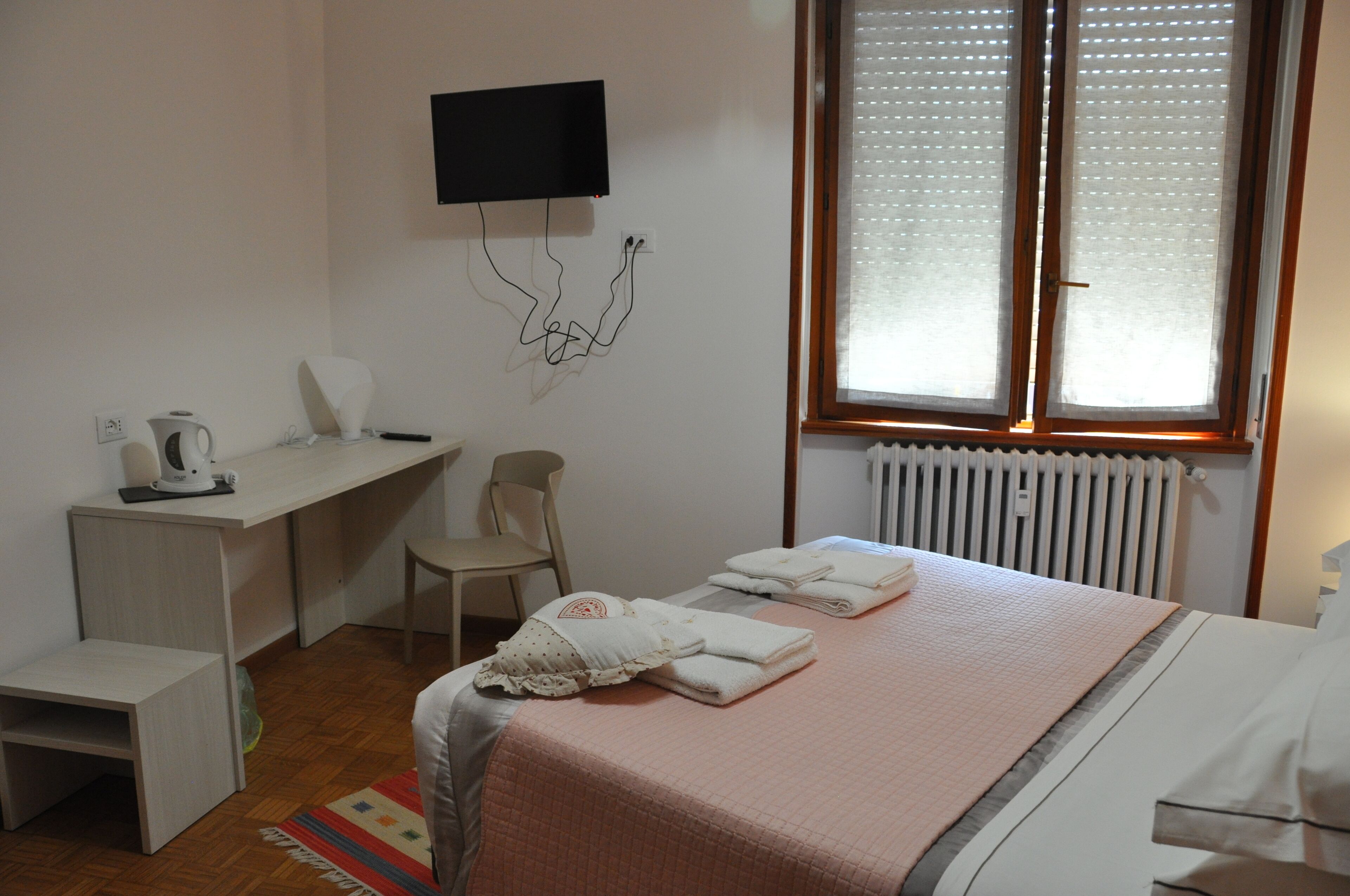 A bedroom with a bed, a desk, a chair, a radiator, and a TV mounted on the wall.