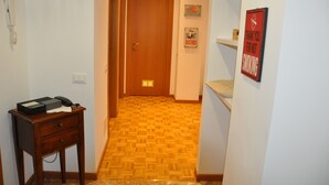 Un couloir avec un plancher en bois, une porte au fond et une petite table sur laquelle se trouvent un téléphone et une boîte.
