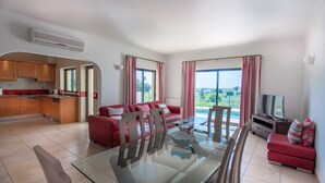 A modern living room with a glass dining table, red sofas, and a TV. - 3 bed, 3 bathroom villa with private pool.  Sea view and BBQ area. (Lagos)