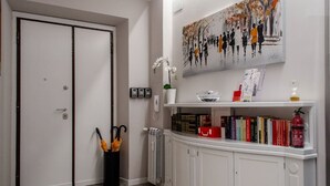 A hotel room with a white door, a radiator, a bookshelf with books, a painting on the wall, and a vase with an orchid. - Interior 1 Ciampino Rome with private balcony (CIAMPINO)