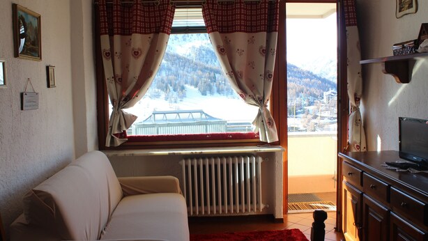 A living room with a sofa, a radiator, a window with curtains, and a view of a snowy landscape. - APARTMENT WITH IDEAL PANORAMIC VIEW FOR FAMILIES (Sestriere)
