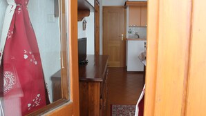 A hallway with a wooden cabinet, a television, and a door leading to a kitchen. - APARTMENT WITH IDEAL PANORAMIC VIEW FOR FAMILIES (Sestriere)