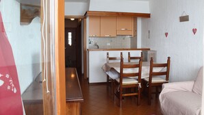 A compact kitchen with wooden cabinets, a dining table with chairs, and a small refrigerator. - APARTMENT WITH IDEAL PANORAMIC VIEW FOR FAMILIES (Sestriere)