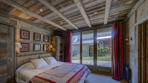 A wooden cabin bedroom with a large bed, a sliding glass door to a patio, and framed pictures on the wall. - Beautiful 4* flat in a chalet with shared sauna, 300 meters from the slopes   (Les Avanchers-Valmorel)