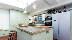 A modern kitchen with a central island, a built-in oven, and a refrigerator. - East London Elegance, by Veeve (London)