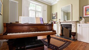A grand piano in a room with a fireplace, a radiator, and a large mirror on the wall. - East London Elegance, by Veeve (London)