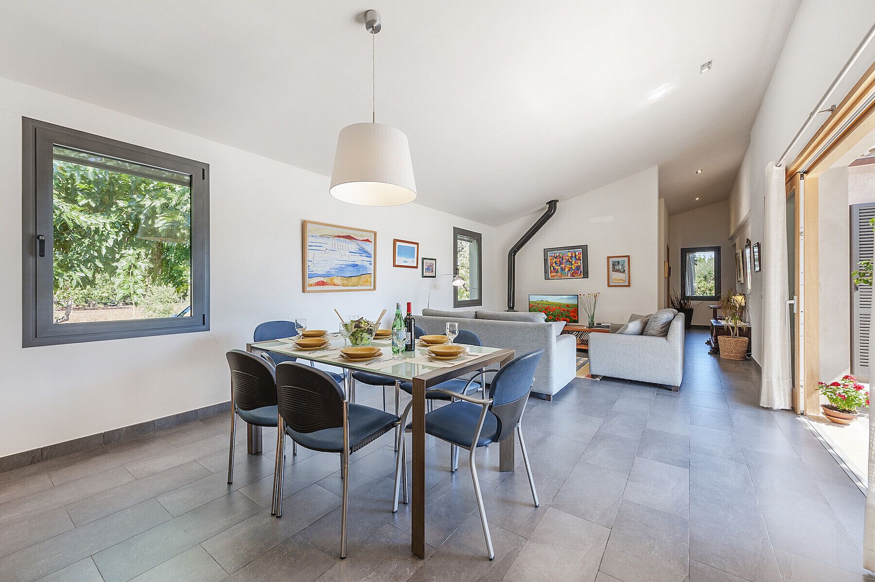 Un espace repas moderne avec une table en verre, des chaises bleues et un canapé gris en arrière-plan.