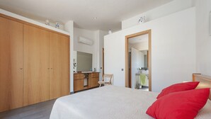Une chambre avec un grand lit, une armoire en bois et une salle de bain visible à travers une porte ouverte.