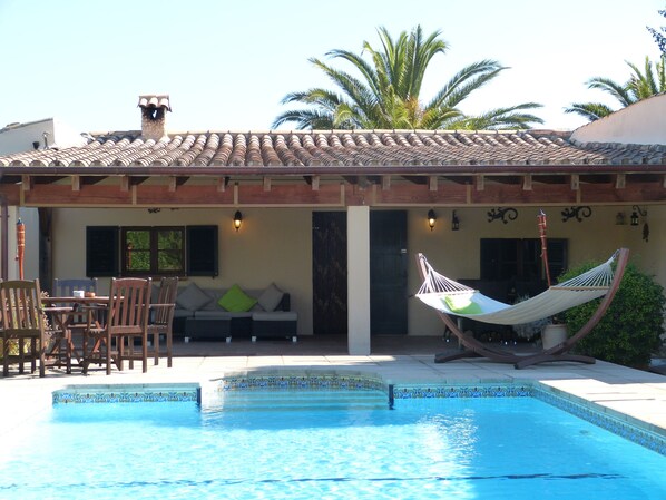 A pool area with a hammock, wooden furniture, and a tiled roof.