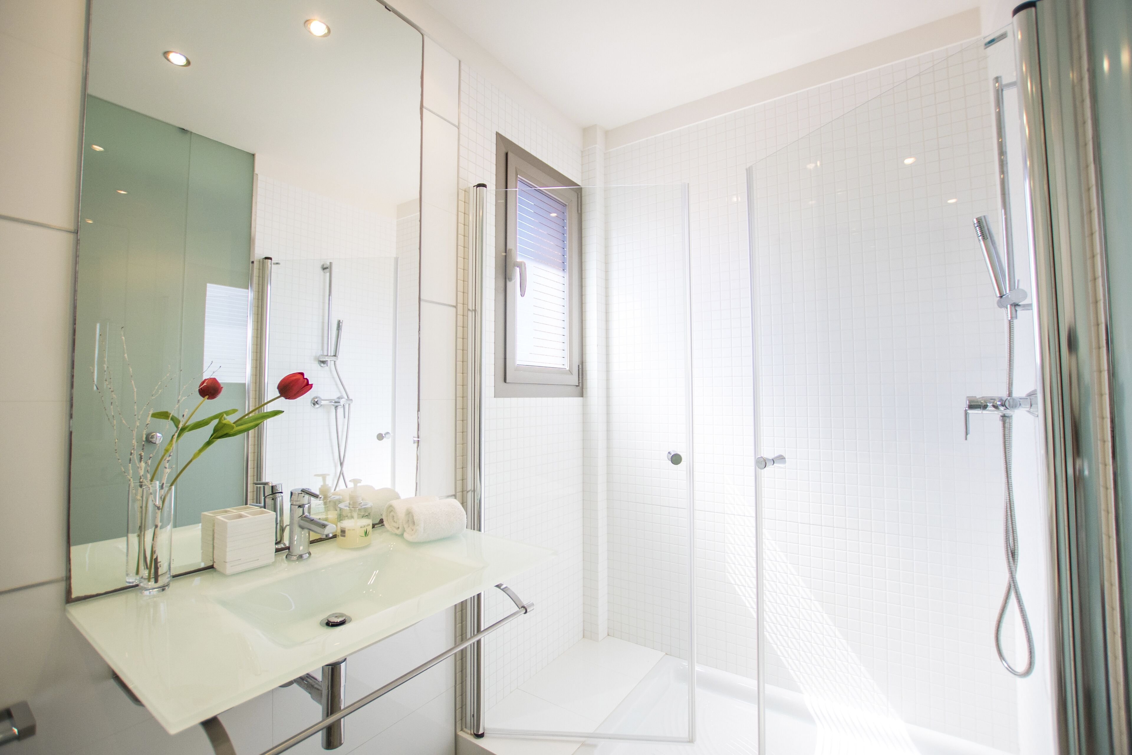 A modern bathroom with a glass shower enclosure, a white sink with a mirror, and a vase with flowers.