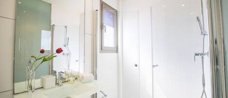 A modern bathroom with a glass shower enclosure, a white sink with a mirror, and a vase with flowers.