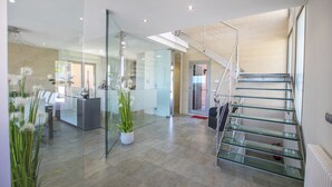 A modern interior with a reception desk, a staircase with glass railings, and a potted plant. - Luxury house on the front line of the sea (Son Serra de Marina)