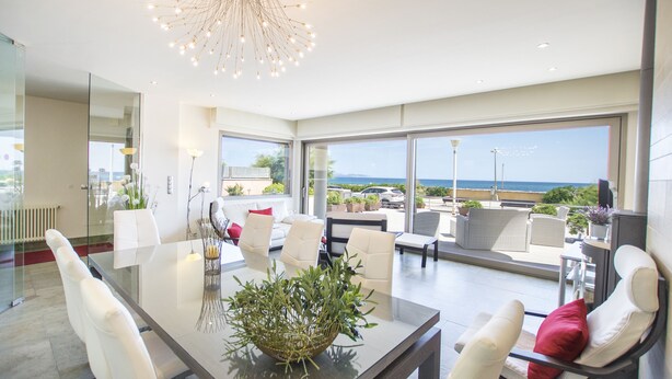 A modern dining area with a glass table, white chairs, and a view of the sea. - Luxury house on the front line of the sea (Son Serra de Marina)