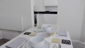 Una mesa de comedor dispuesta con pulcritud, con platos, cuencos, cubiertos y servilletas blancos.