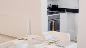 Un comedor con una mesa blanca dispuesta para dos, con platos, tazones, cubiertos y un vaso de agua.