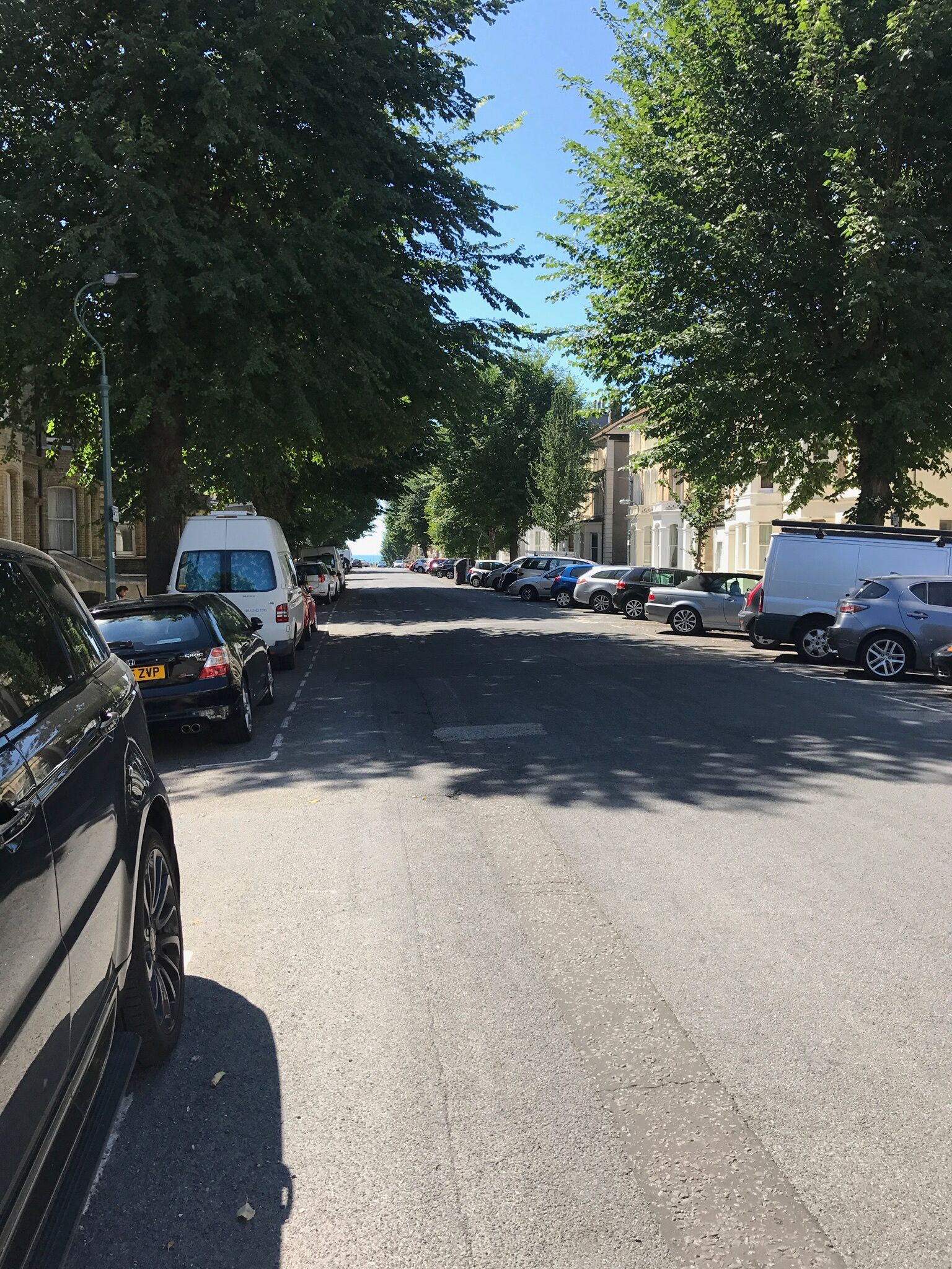Une rue bordée de voitures garées et d’arbres, avec des immeubles de chaque côté.