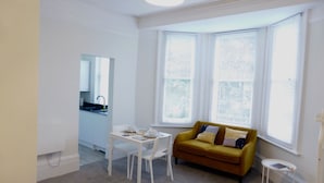 Una habitación compacta con una cama, un sofá amarillo, una mesita y una ventana con persianas.