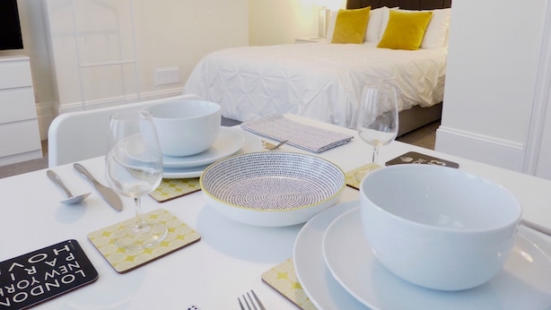 Una habitación de hotel ordenada con una cama, una mesa de comedor puesta con platos, tazones, cubiertos y vasos.