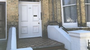 Un edificio tradicional de ladrillo con una puerta blanca numerada 24, una pequeña escalera que conduce a la entrada y una ventana con cortina.
