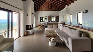 Amplia sala de estar con techo alto, un sofá grande, una mesa de comedor y una cocina al fondo.