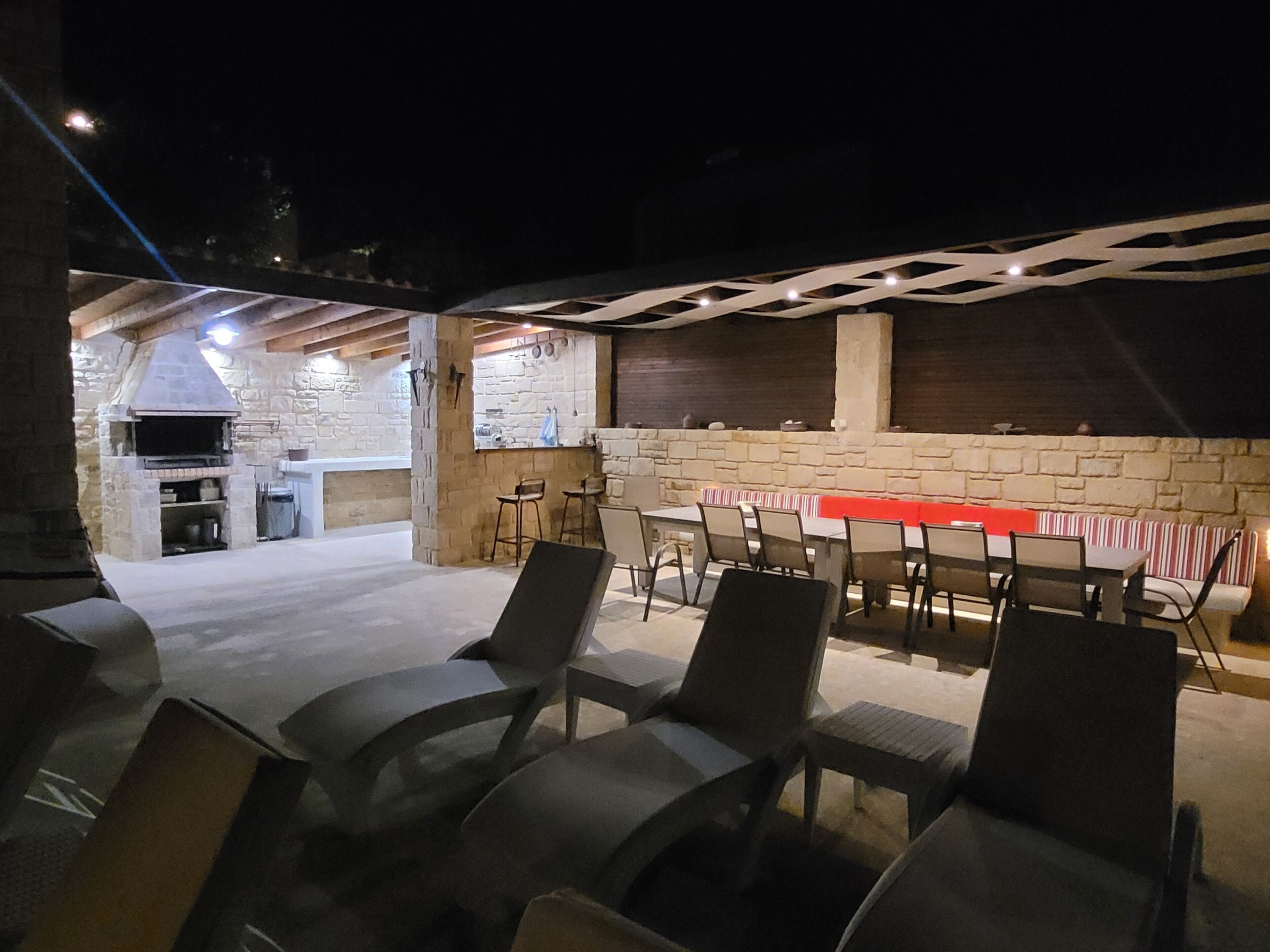 Un patio al aire libre con paredes de piedra, un horno de ladrillo y una larga mesa con sillas.