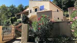 A two-story house with a balcony, a gate, and a small garden with pink flowers. - Large fully air conditioned luxury villa with pool in beautiful location (Reynès)