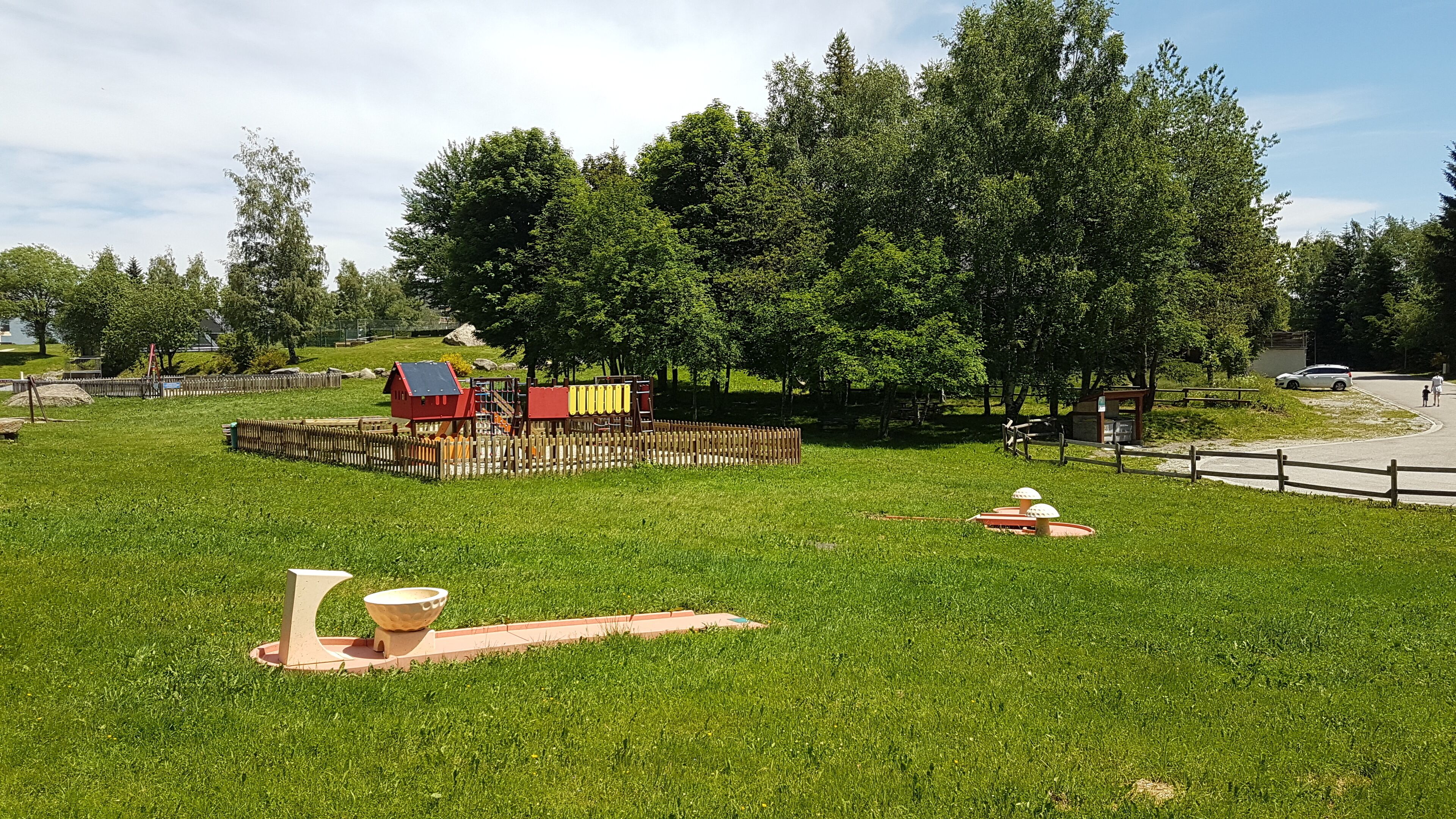 A park with a playground, picnic tables, and a red building.