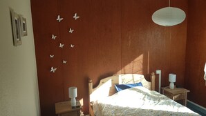 A bedroom with a wooden headboard, a bed with patterned bedding, two bedside tables with lamps, and wall decorations including butterflies. - Appt T4, 8 pers, 84m2 in chalet in calm close tracks, Ax 3 Domaines Bonascre (Ax-Les-Thermes)