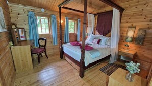 Un dormitori de cabana de fusta amb un llit amb cortines, un escriptori de fusta, una cadira i una tauleta de nit amb una làmpada.