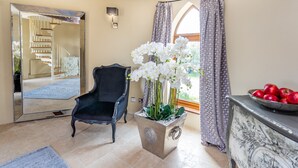 Une pièce avec un grand miroir, une chaise noire, une orchidée en pot, une fenêtre avec des rideaux et une table en marbre sur laquelle sont posées des pommes.