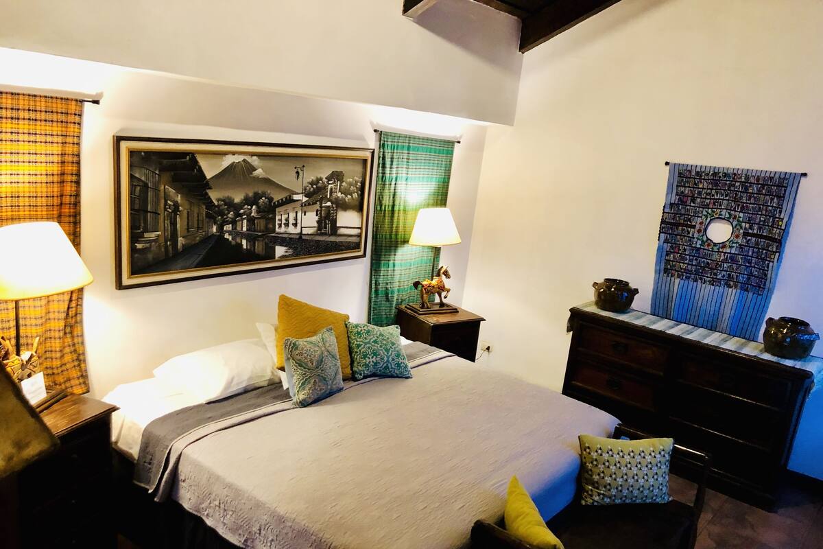 A neatly arranged bedroom with a bed, bedside tables, a dresser, and a wall-mounted picture.
