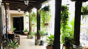 A covered outdoor area with tiled flooring, potted plants, and hanging planters. - Hotel La Casa de Don Moncho (Antigua Guatemala)