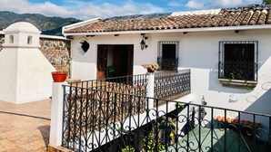 A white building with a tiled roof, a balcony with wrought iron railings, and a view of mountains in the background. - Hotel La Casa de Don Moncho (Antigua Guatemala)