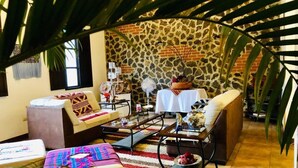 A cozy living room with a stone wall, a coffee table, a sofa, and a dining table. - Hotel La Casa de Don Moncho (Antigua Guatemala)