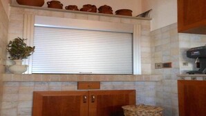 Una cocina con salpicadero de piedra, armarios de madera, una ventana con persiana enrollable y una cafetera.