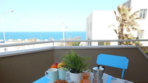 Un balcón con una mesa dispuesta para el desayuno, incluyendo cruasanes, fruta y una cafetera.