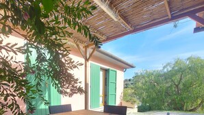 An outdoor patio with a wooden table and wicker chairs, a green door, and a bamboo ceiling structure.