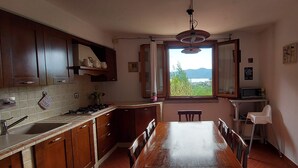 A kitchen with wooden cabinets, a dining table, and a view of greenery and mountains through a window.