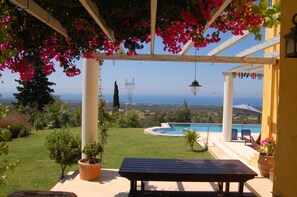 Une terrasse avec une piscine, une vue sur la mer et une pergola ornée de fleurs.