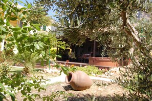 Un jardin avec un grand pot en argile, diverses plantes et un bâtiment en arrière-plan.