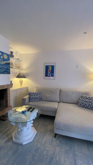 A living room with a sofa, patterned cushions, a glass coffee table, a lamp, and a framed picture on the wall.