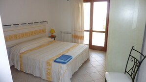 Un dormitori amb un llit, una petita taula de nit, una cadira i una finestra amb cortines.