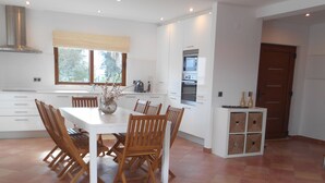 Une cuisine spacieuse avec des meubles blancs, une table à manger avec des chaises et une grande fenêtre.
