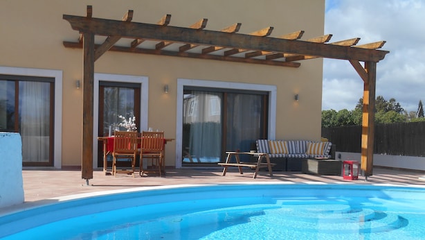 Une piscine agrémentée d’une pergola en bois, d’un espace salon extérieur et d’un patio couvert.