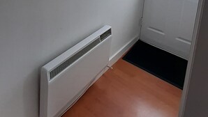 A room with a white radiator, a framed picture with a heart-shaped arrangement of stones, and a door with a window. - 3 bedroom holiday bungalow on the beach front, Point Clear Essex (Clacton)