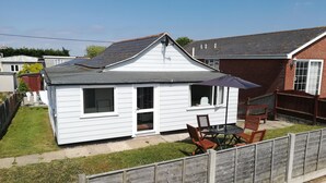 A small white house with a dark roof, a fenced backyard, and a patio with a table and chairs. - 3 bedroom holiday bungalow on the beach front, Point Clear Essex (Clacton)