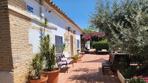 A courtyard with a tiled floor, potted plants, outdoor furniture, and a white building with stone walls. - Spacious Seville Cortijo with large private pool set in orange groves free wifi (Lora Del Rio)