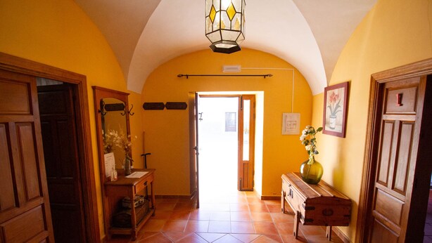 A hallway with a tiled floor, wooden doors, a bench, and a vase with flowers.