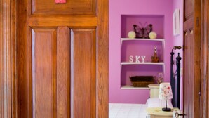 A wooden door with a number '1' sign, a pink wall, a bed, a nightstand, a lamp, and shelves with decorative items.
