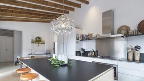 A modern kitchen with a large island, wooden stools, a chandelier, and white cabinetry.